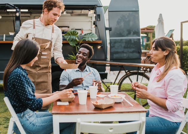 Multiracial friends eating at food truck outdoor during summer vacation