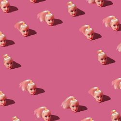Pattern made of doll heads on pink background
