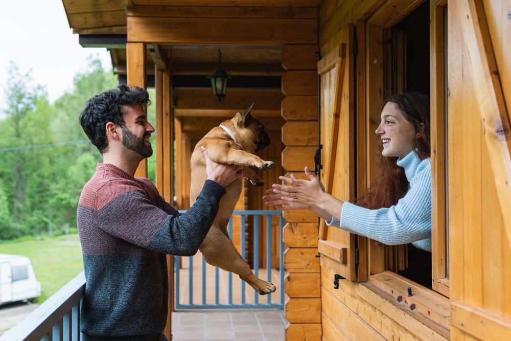 Cheerful couple playing with dog on terrace of house