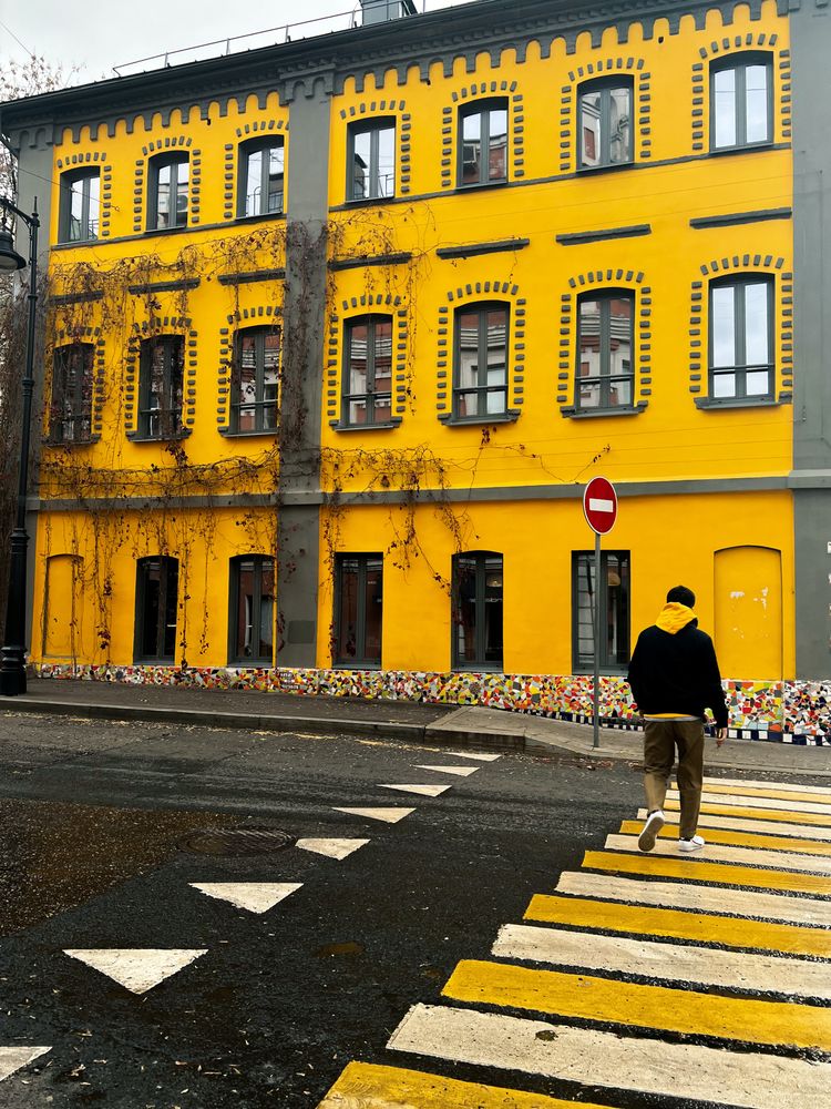 Back view of man in hoodie walking on pedestrian lane beside yellow building