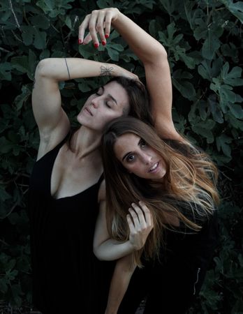 Young women posing near green bush