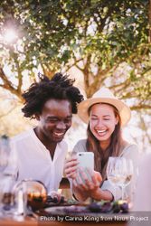 A man and woman laughing at something on the phone screen over lunch outdoors E4A360