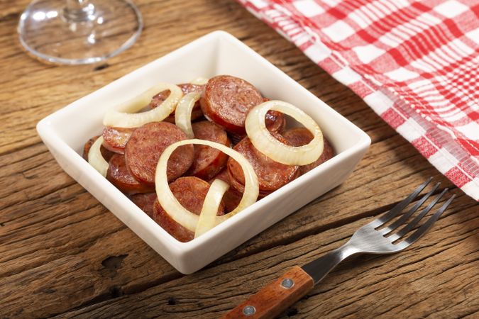 Sliced calabrese sausage with onion on wooden background.