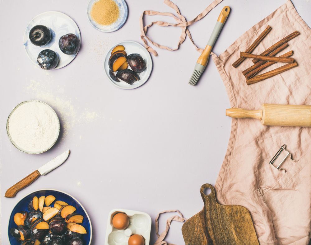 Baking ingredients and tools, plums, pastry brush, cinnamon, eggs on pastel background, copy space