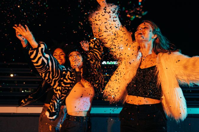 Multi-ethnic group of women throwing confetti at night in the city