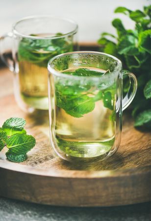 Close up of mint tea with fresh mint leaves on wooden tray, vertical composition