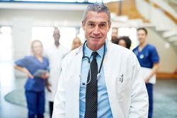 Portrait of mature doctor in lab coat and stethoscope with his medical team in the background