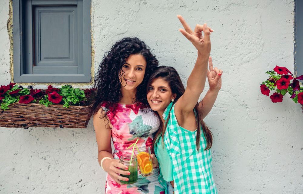 Two female friends making peace sign with fruity cocktails