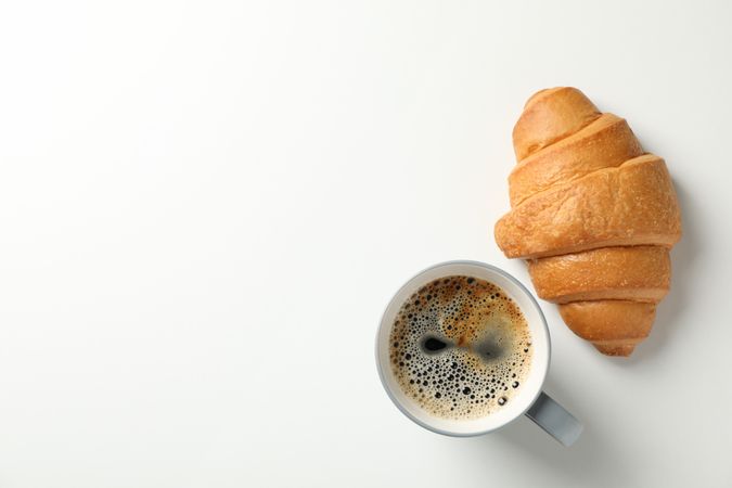 Croissant and ceramic cup of coffee on plain background, space for text