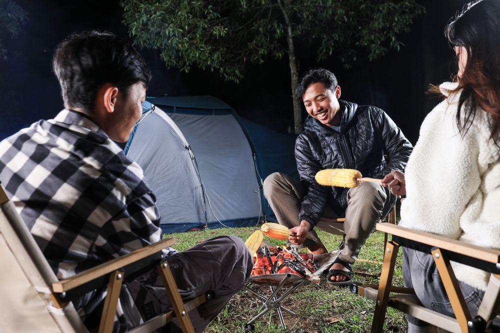 Asian Young Man Grilling Corn on Campfire