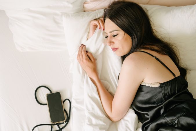 Dreamy woman sleeping near cellphone on bed