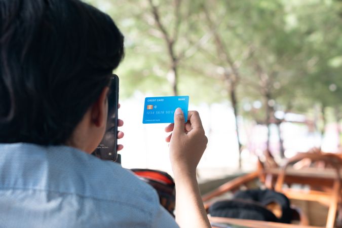 Back View Happy Asian Young businessman hold blue creditcard and phone purchasing online shopping in outdoor cafe.
