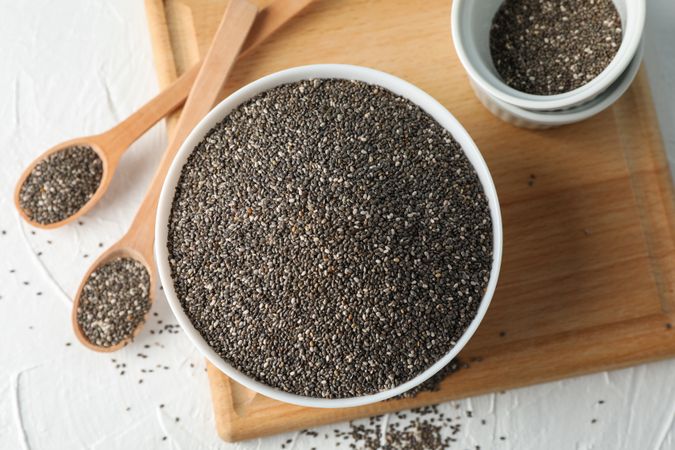 Bowl and spoons with chia on plain background, top view