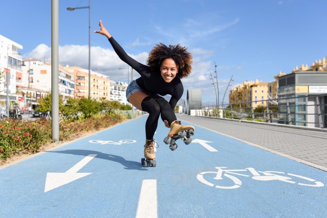 Smiling female with afro hairstyle rollerblading on one leg