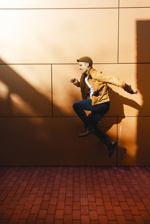 Confident guy jumping near modern wall