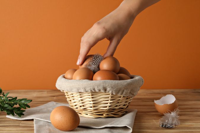 Eggs in a wicker basket, with a hand, on an orange background.