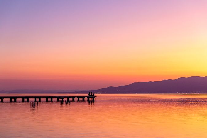 Anonymous tourists sitting on pier during sundown