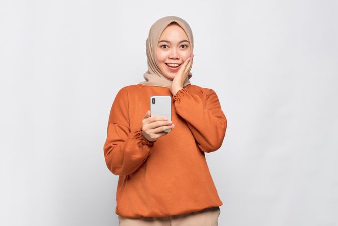 Muslim woman with hand on cheek while taking photo on  smart phone