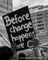 Grayscale photo of person holding banner with " Before the change happens here" bxMzv0