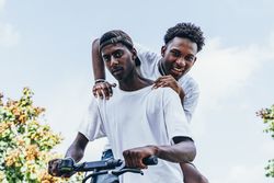 Black man riding on electric scooter in park with friend on back