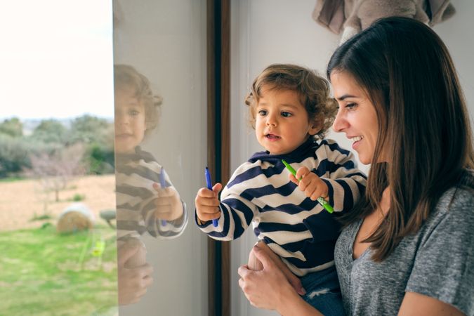 Happy woman and toddler looking out window together