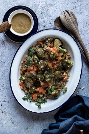 Braised brussels sprouts and pumpkin with quinoa in bowl near cup of sauce