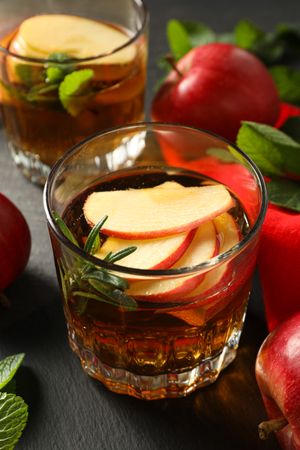 Glasses with apple cider, mint leaves and red apples on dark wooden background, close up