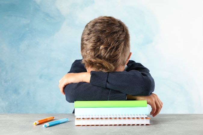 Boy sleeps on notebooks heap against color background, space for text