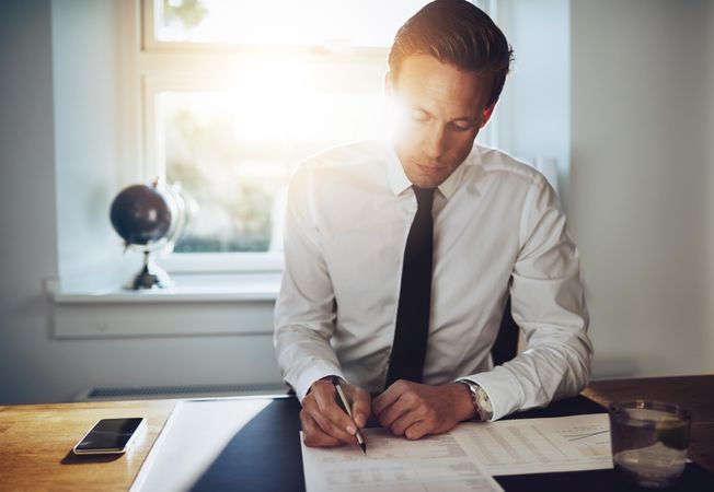 Man in shirt and tie working on papers in sunny office