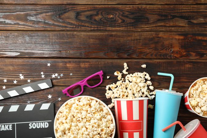 Flat lay. Buckets with popcorn, clapperboard, 3d glasses and drinks on wood background