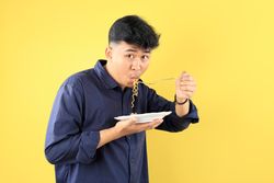 Indonesian Young Student Eating Instant Noodle using Stainless Fork.