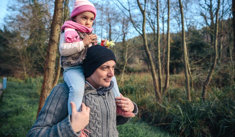 Father carrying daughter on shoulders in forest