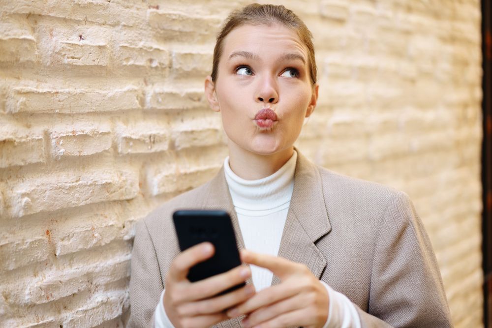A Young Woman Joyfully and Playfully Posing with Her Phone Against a Textured Wall