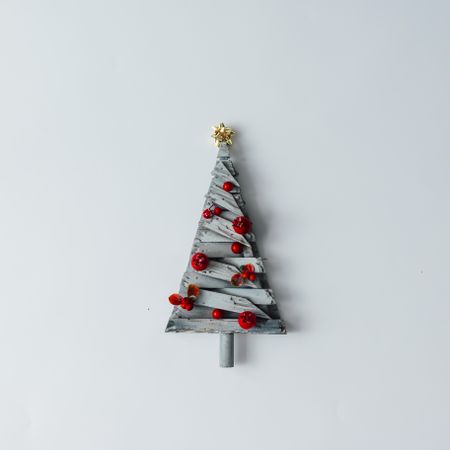 Decorative star topped wooden Christmas tree with red baubles on light background