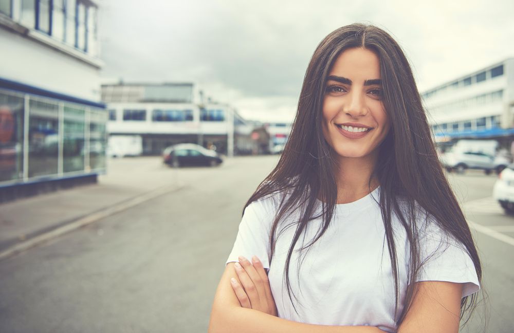 Portrait of content brunette woman standing outside in parking lot