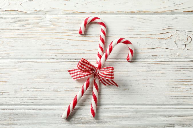 Sweet candy canes with bows on wooden background, space for text