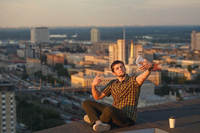 Male taking photo of himself sitting on roof with takeaway coffee cup