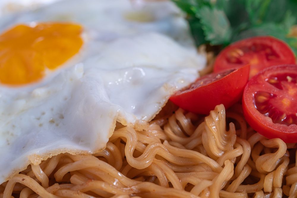 A plate of noodles with an egg and tomato on top