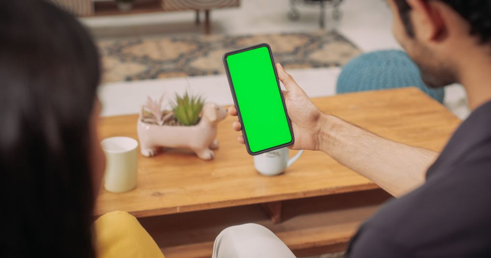 Over the Shoulder Indian Couple Using Smartphone with Green Chroma Key Screen