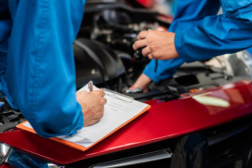Two male auto mechanics standing working at open engine with clipboard