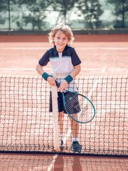 Smiling kid standing near net on court after playing tennis
