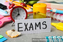 The word “Exams” surrounded by clock and stationary on desk bEjnl0
