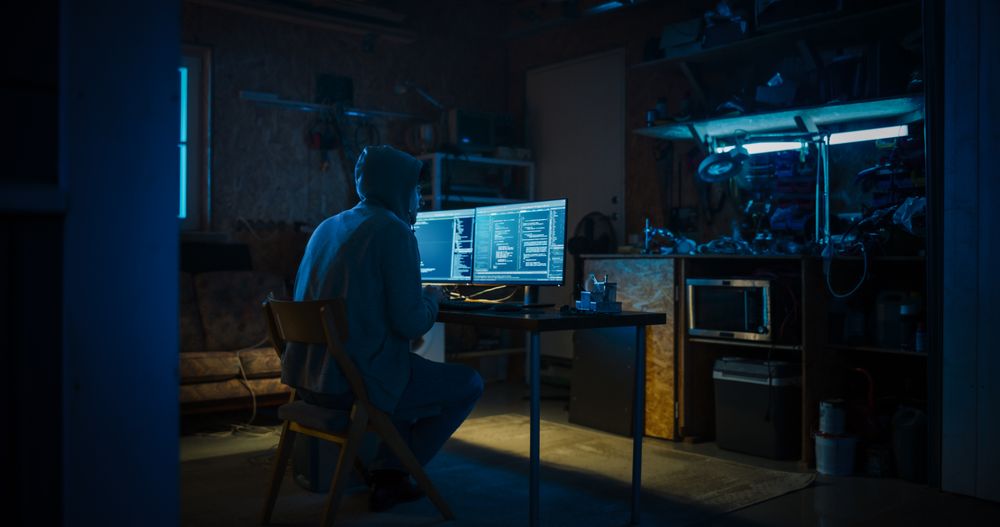 Backview Of Anonymous Professional Programmer Obsessively Writing a Code on His Desktop Computer, Late at Night In Garage.