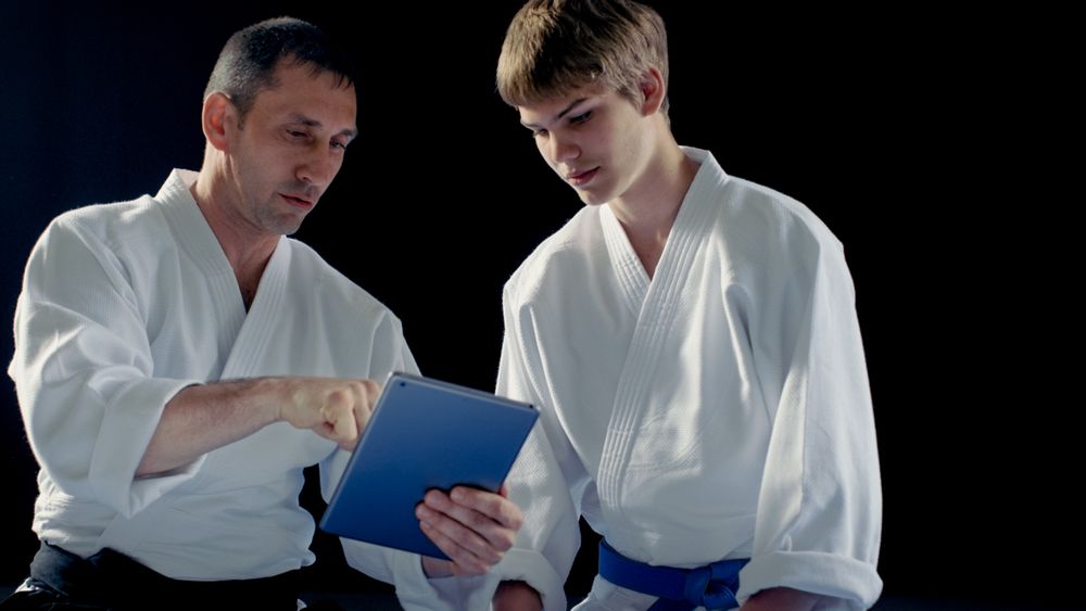 Martial Arts Master Wearing Hakamas Teaches Young Student Aikido Technique with the Help of the Tablet Computer.