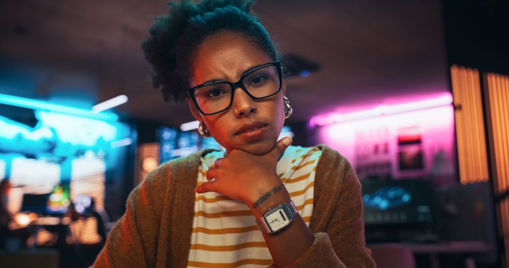 Stylish Young Black Woman Looking at Camera With Confusion While Working on Desktop Computer in Creative Office.