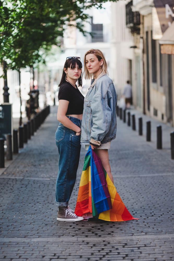 Lesbian couple with LGBT flag standing on street