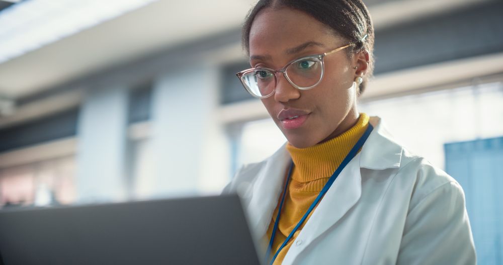 Portrait of Young Black Female Expert in a Lab Coat Smiling and Using Laptop Computer.