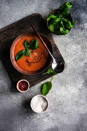 Tomato soup served with oil garnish and herbs, peppers and salt