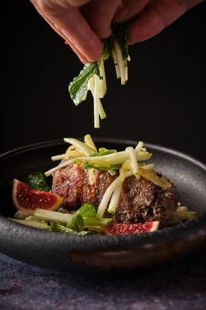 Crop person adding chopped veggies to pig trotter