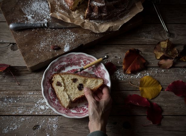 Crop hands holding piece of Kugelhopf near autumn leaves